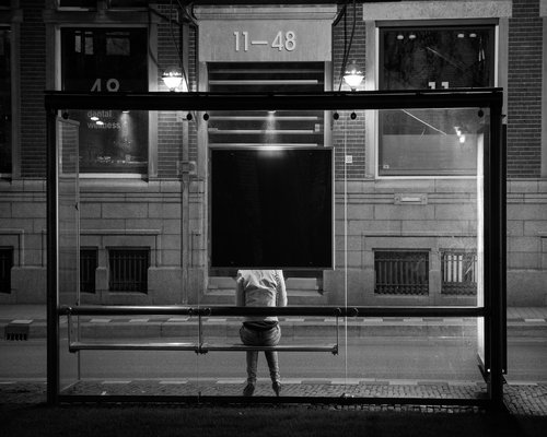 A person waiting at a city bus stop in the early morning